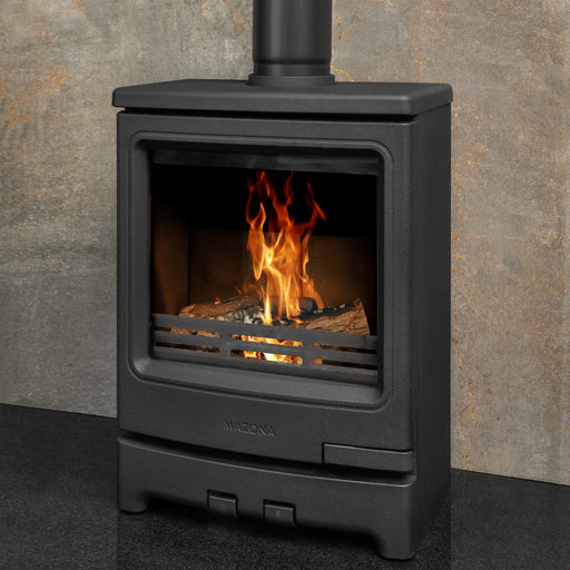 Black freestanding stove with flames inside, against a stone wall.