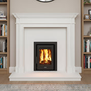 White fireplace with a lit fire, round mirror above, bookshelves on either side, and a rug on the floor.