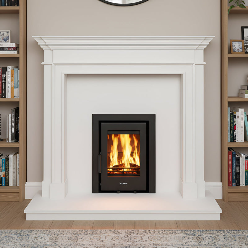 White fireplace with a lit fire, round mirror above, bookshelves on either side, and a rug on the floor.