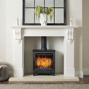White fireplace with a lit Mazona Woodburning Stove, decorative mirror above, and a small table with a blanket and vase to the left.