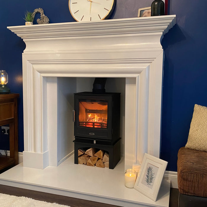 White fireplace with a black stove insert, clock, and decorative items against a blue wall.