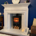 White fireplace with a black stove insert, clock, and decorative items against a blue wall.