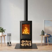 A black wood-burning stove with an open fire and visible flames, set in a modern living room with a light gray wall, wood flooring, and decorative side tables.