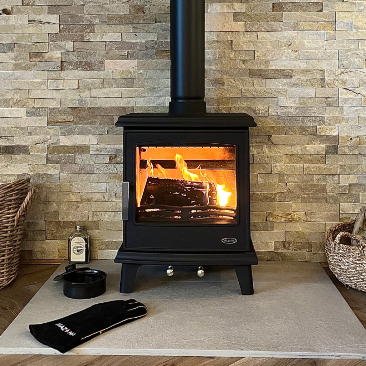 Black freestanding stove with flames inside, placed against a brick wall.
