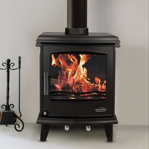 Black freestanding stove with flames inside, placed against a white wall next to a large window.