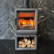 Grey wood stove with fire and wood inside, against a stone wall background
