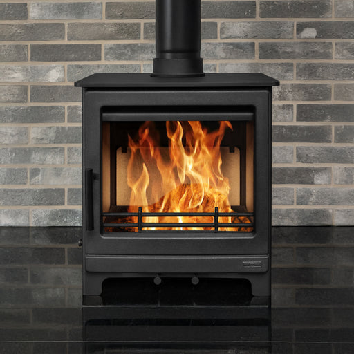 Black stove with flames burning inside against a gray brick wall.