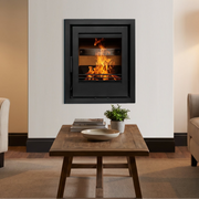 A modern black fireplace insert mounted on a white wall in a styled living room with a beige armchair, a wooden coffee table, a sofa, and a floor lamp.