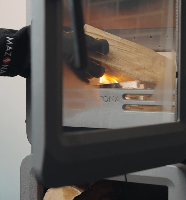Person lighting a fire in a Mazona wood stove with a black glove.